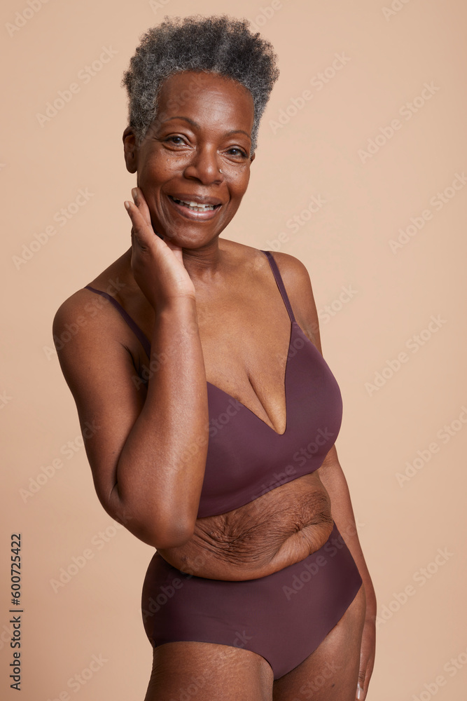 Studio shot of smiling senior woman posing in underwear against beige background Studio shot of smiling senior woman posing in underwear against beige background