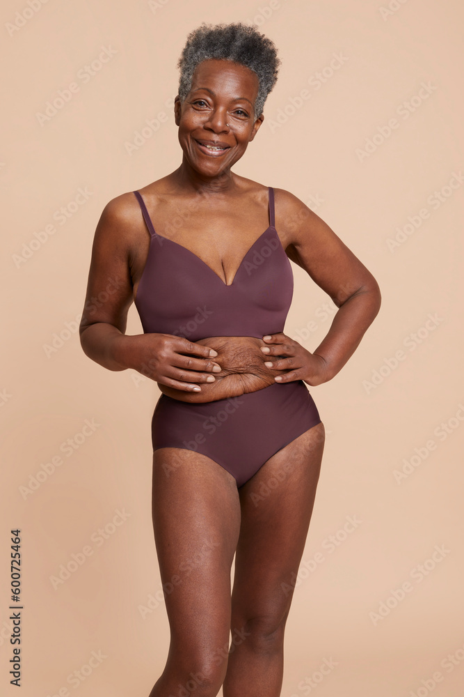 Studio shot of senior woman posing in underwear against beige background