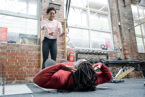 Daughter helping mother practicing sit-ups in gym