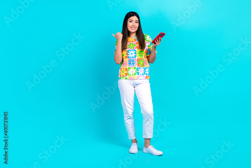 Full length cadre of chinese young blogger girl hold phone point finger empty space website interface isolated on cyan color background