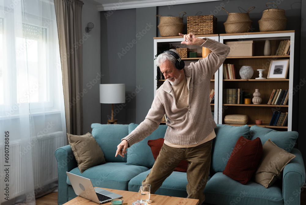 Happy senior old grandfather man in wireless headphones dancing, singing at home, choosing favorite energetic disco music in mobile application, entertaining indoors. Retired people relax activities - obrazy, fototapety, plakaty 
