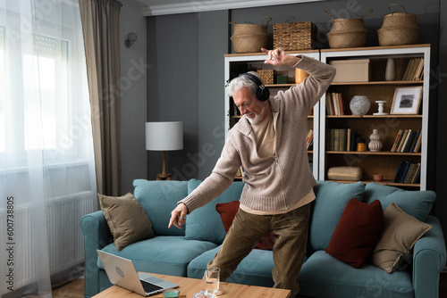 Canvastavla Happy senior old grandfather man in wireless headphones dancing, singing at home, choosing favorite energetic disco music in mobile application, entertaining indoors