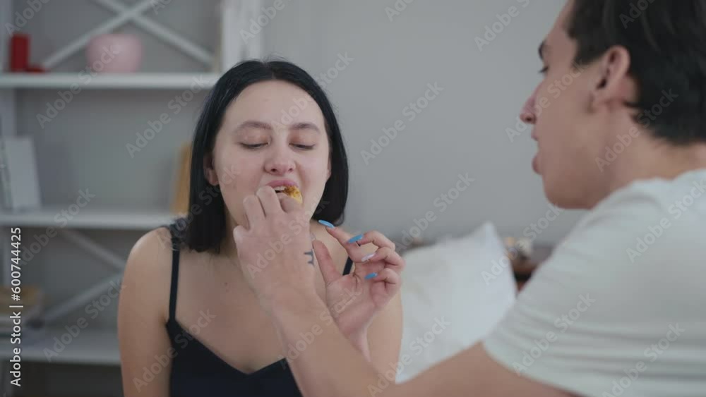 Portrait of charming Caucasian young girlfriend smiling as boyfriend feeding partner with croissant. Happy woman enjoying Valentine's morning with man in bedroom at home Portrait of charming Caucasian young girlfriend smiling as boyfriend feeding partner with croissant. Happy woman enjoying Valentine's morning with man in bedroom at home
