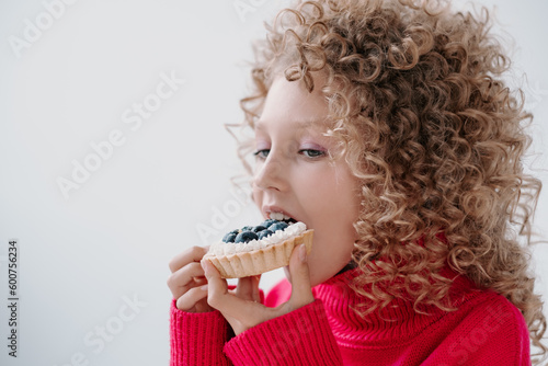 a girl in a pink sweater and afro curls eats a festive cupcake
