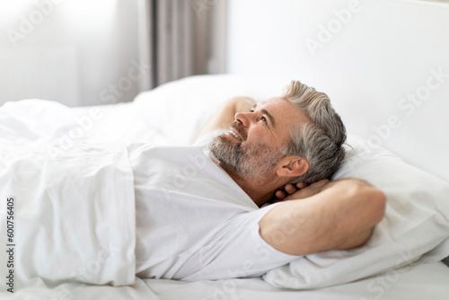 Side view of happy adult man smiling in bed