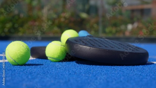 Padel rackets on the blue padel court while a yellow ball rolls towards them.