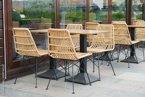 Empty tables and plastic wicker chairs on the summer terrace near a small cafe. The restaurant is open and waiting for guests. Cafeteria furniture outside.