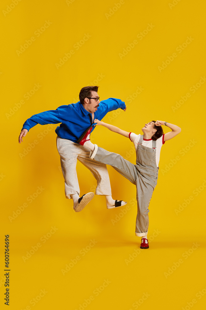 Portrait with funny couple, woman and man playfully arguing over yellow studio background. Fight in motion