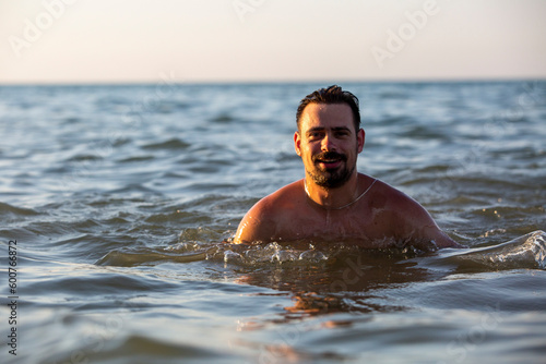 A happy smiling man swims in the sea during sunset