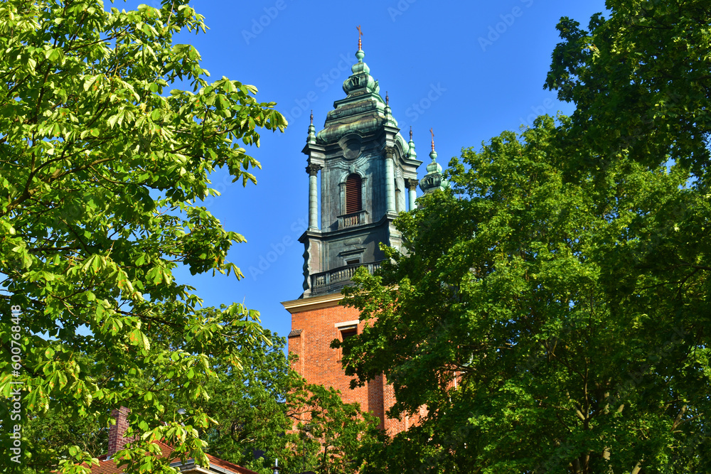 Cathedral towers with a green top in the background of blue sky, trees around. A sunny summer day. Cathedral on the Tymsky island. Poland, Poznan, June 2022.