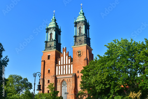 Catholic church with green top of cathedral towers in the background of blue sky, trees around. A sunny summer day. Cathedral on the Tymsky island. Poland, Poznan, June 2022.