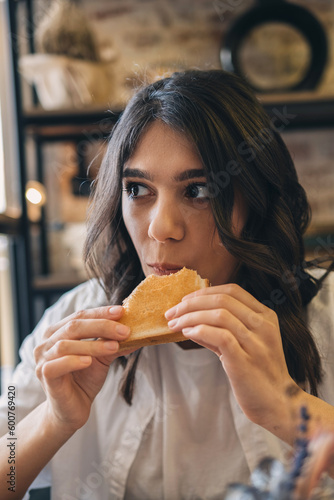 Portrait of a young attractive dark-haired woman eating a sandwich in a cafe.
