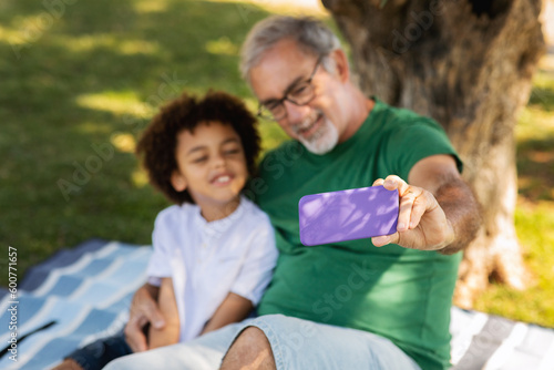 Cheerful little mixed race boy and old caucasian grandfather take selfie on smartphone, enjoy free time