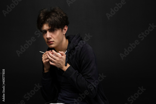 A homeless young person with bruises under their eyes in dirty, tattered clothing, greedily holding a paper bowl of food. Isolated on black background.