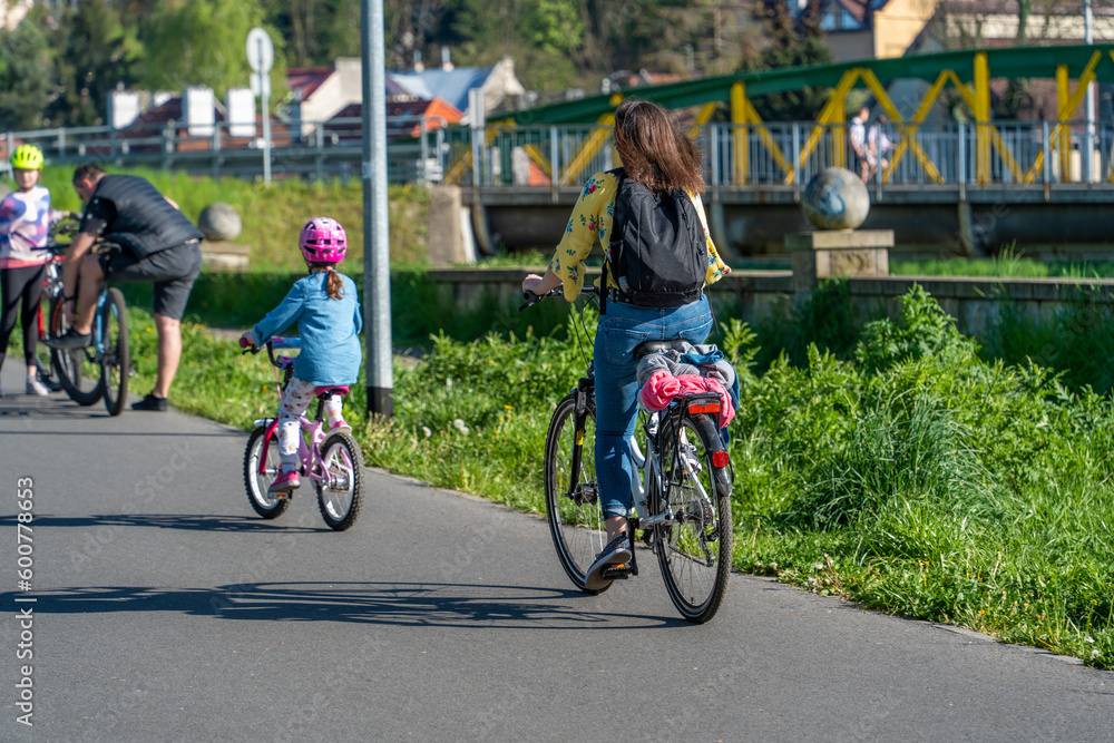 Fototapeta premium Authentic group of people riding bikes down the street on a sunny day, trending photo, mother and child, father and child, wide green lanes, long shade, sustainable eco-friendly transportation