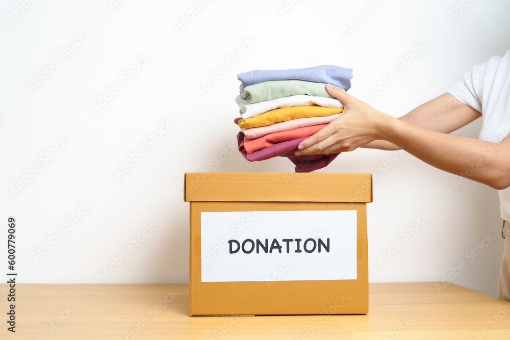 Donation, Charity, Volunteer, Giving and Delivery Concept. Hand holding  Clothes into Donation box at home or office for support and help poor,  refugee and homeless people. Copy space for text Stock Photo