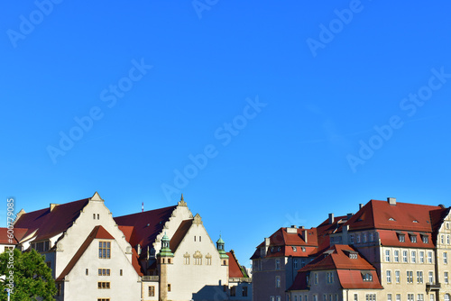 Old buildings with beige walls and red roofs on the horizon, and a wide background of blue cloudless sky. Ancient architecture. Cityscape view. Sunny summer day. Poland, Poznan, July 2022.
