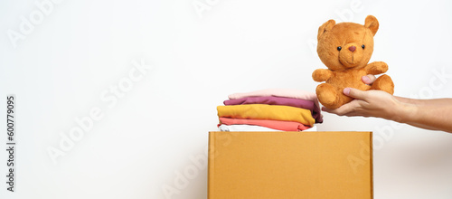 Kid Donation, Charity, Volunteer, Giving and Delivery Concept. Hand donate Bear doll and Clothes into cardboard box at home for support and help poor, refugee and homeless people. Copy space for text © Jo Panuwat D
