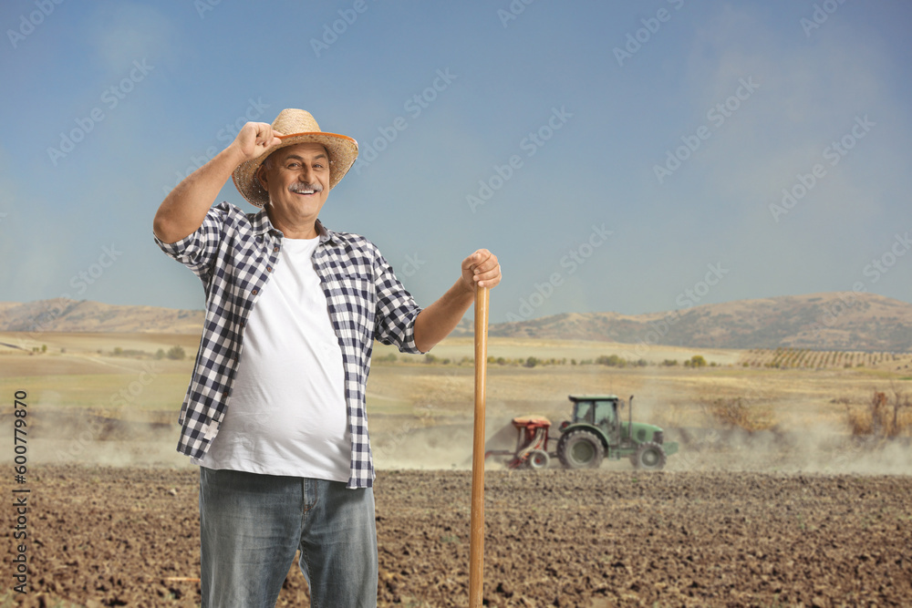 Portrait of a happy mature farmer with a shovel standing on a field with tractor