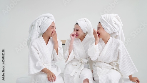 Three young beautiful asian women in bathrobes and towels on heads sitting enjoy chatting. Female best friends in gowns and towels having fun