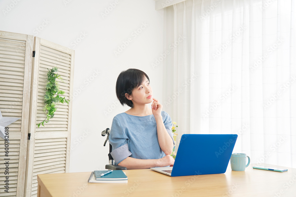 リビングでノートパソコンの前で考える車椅子に乗った女性 リビングでノートパソコンの前で考える車椅子に乗った女性