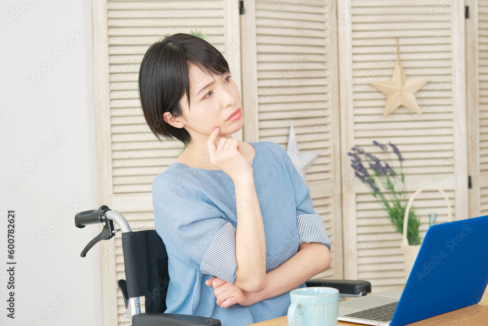 リビングでノートパソコンの前で考える車椅子に乗った女性 リビングでノートパソコンの前で考える車椅子に乗った女性