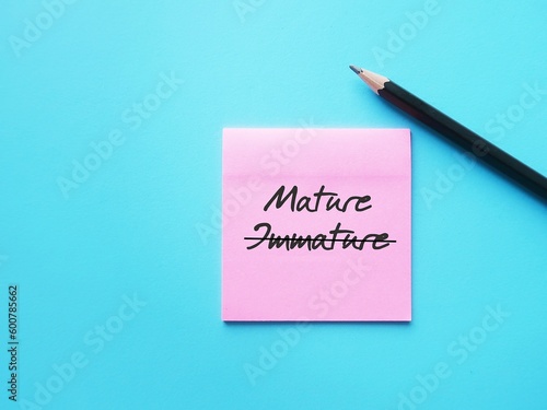 Note paper on blue background with handwritten text cross off IMMATURE to MATURE, means to improve from being person who thinks and acts like child to be immature, think and act like adult
