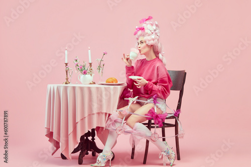Portrait of elegant princess, queen wearing pink clothes, and wig drinking coffee over pink background. Royalty breakfast photo