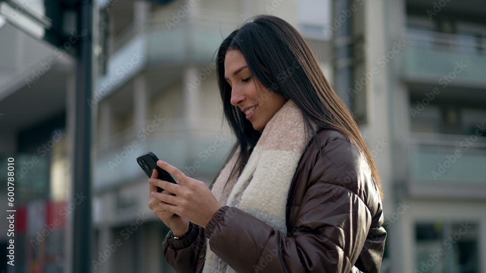 Happy adult girl in 20s holding cellphone in city street. Tracking shot in motion of a young woman reading message on phone standing outside in urban setting Happy adult girl in 20s holding cellphone in city street. Tracking shot in motion of a young woman reading message on phone standing outside in urban setting