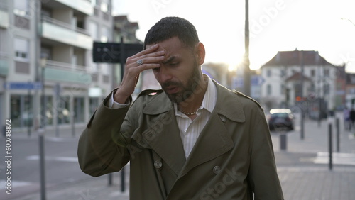 Frustrated young man walking in city street feeling disbelief. One Male Middle Eastern person walks in sidewalk suffering from regret and anxiety