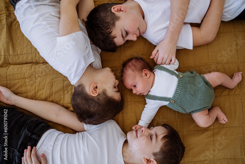 Foto Three big brothers with their little newborn brother lying in bed