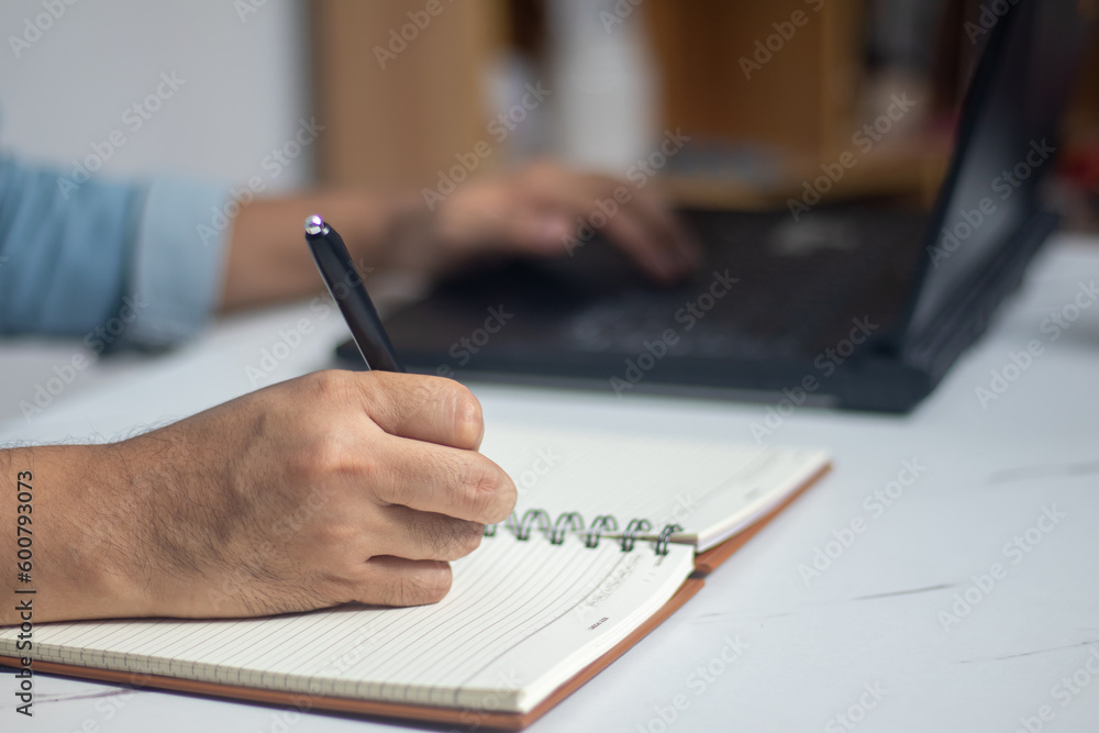 Male hand writing a note in a notebook concept of business people working Male hand writing a note in a notebook concept of business people working