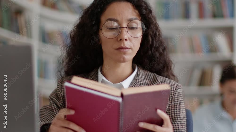 Young smart woman student reading book in college library, studying topic or making research, tracking shot Young smart woman student reading book in college library, studying topic or making research, tracking shot