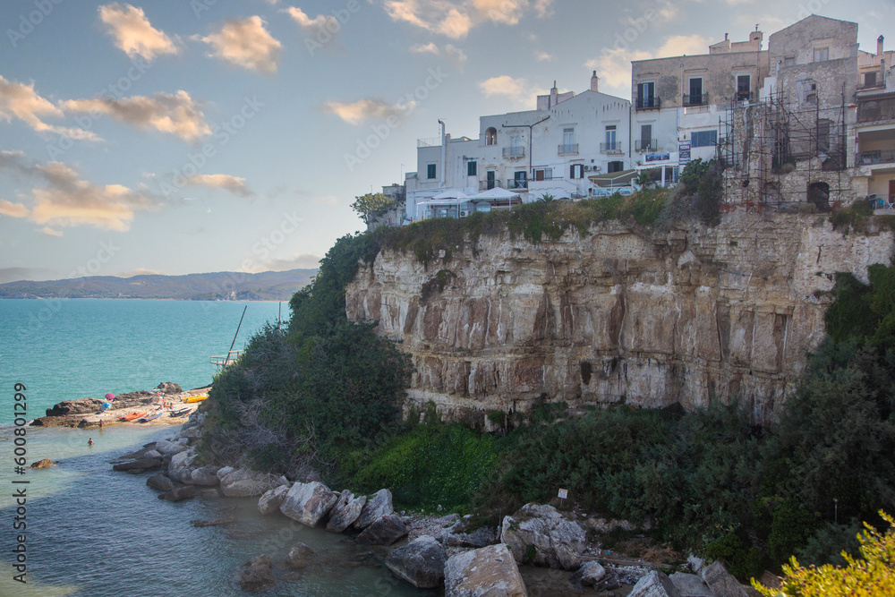 A view of a cliff with houses on it and the sea in the background. Vieste, Puglia, Italy.