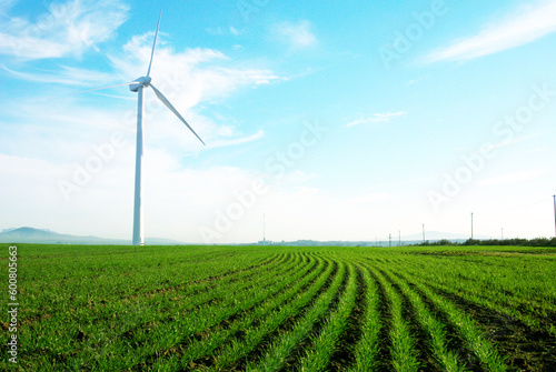 Wind turbine standing against a blue skywith some clouds in a green grass field