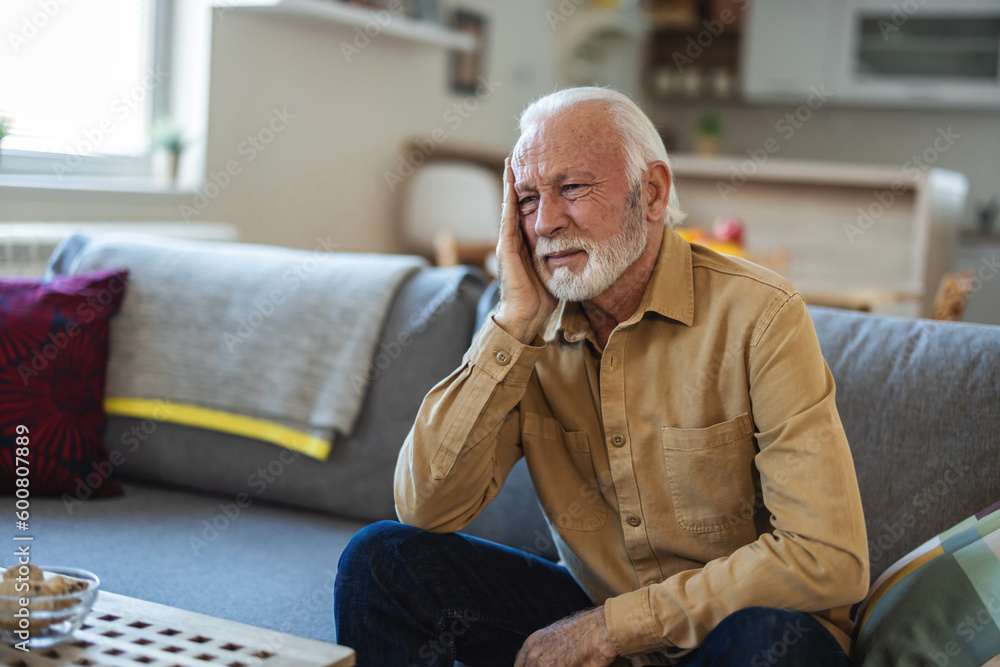 Close-up of senior man having headache. Cropped shot of stressed senior man sitting in the living room. Close-up of senior man having headache. Cropped shot of stressed senior man sitting in the living room.