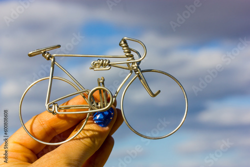 A metal bicycle in a woman's hand against a blue-gray cloudy sky. Holding a toy mini bike. Cycling in mountains. Round aluminum wheels of a bike. Healthy lifestyle, outdoor leisure and sports concept.