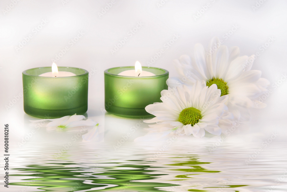 Green candles and daisies near water reflection on dreamy white background