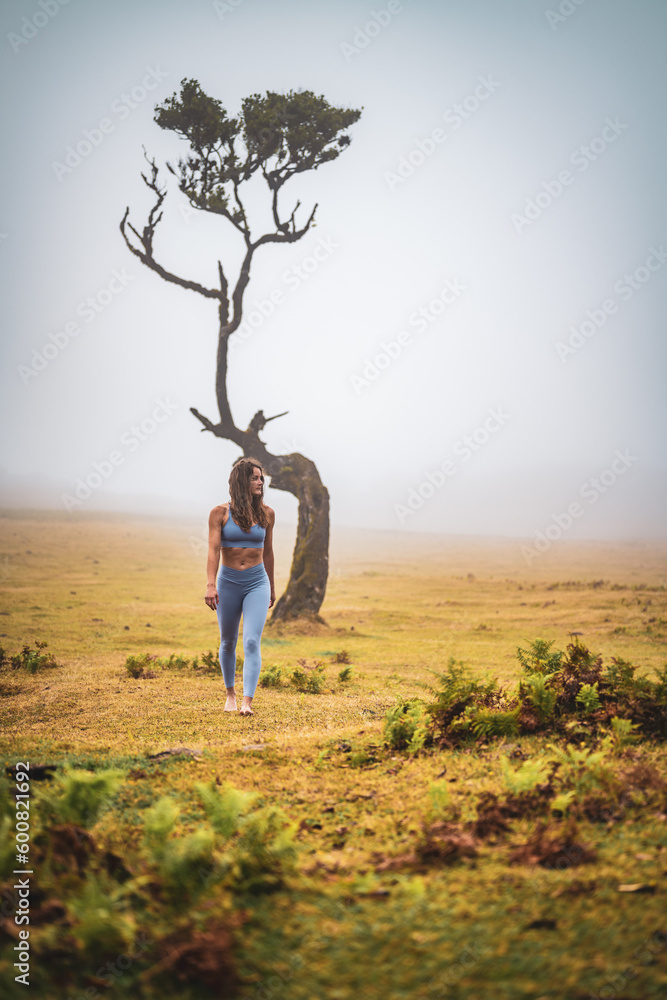 Barefoot woman in sportswear enjoying walk over flat field with laurel tree in foggy atmosphere. Fanal forest, Madeira Island, Portugal, Europe. Barefoot woman in sportswear enjoying walk over flat field with laurel tree in foggy atmosphere. Fanal forest, Madeira Island, Portugal, Europe.