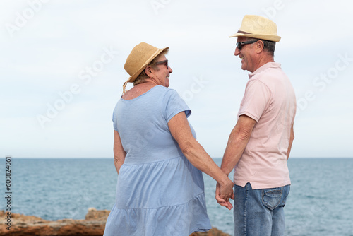 Heterosexual senior couple holding hands and looking each other with the sea on the background.