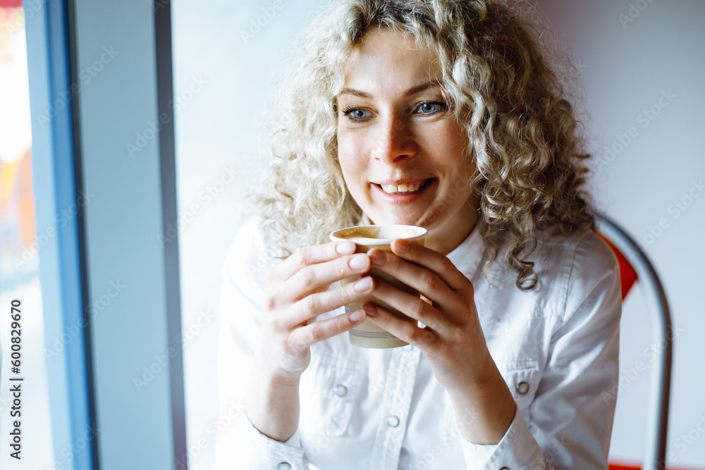 Portrait of charming young business woman with curly hair enjoying cup of coffee during break at work. Coffee break. Rest and pleasure. Positive emotions. Good mood. Happy people. Portrait of charming young business woman with curly hair enjoying cup of coffee during break at work. Coffee break. Rest and pleasure. Positive emotions. Good mood. Happy people.