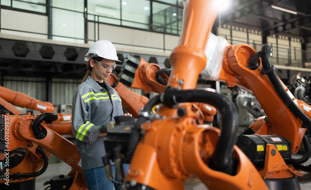 After installing a program on the robotic arm, a female engineer with a robotic arm controller performs a test run. After installing a program on the robotic arm, a female engineer with a robotic arm controller performs a test run.