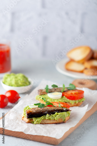Sandwiches with sprats on toasted slices of bread. Sandwich with smoked sprat - fish, avocado and tomato.