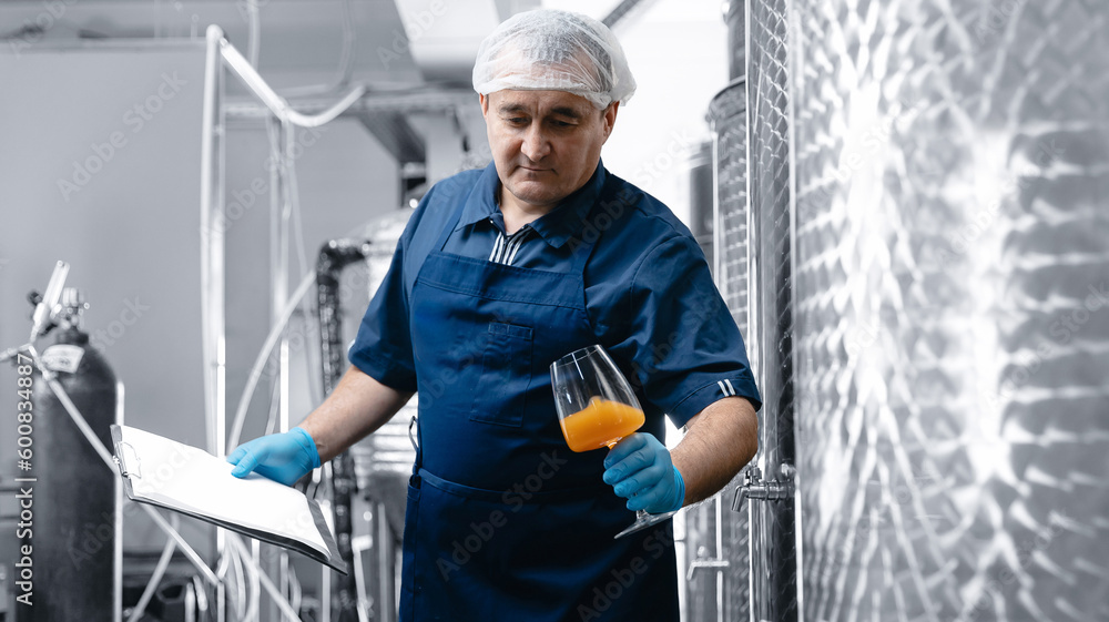 Inspector checking drink in alcohol brewery manufacturing factory. Worker examining quality of craft beer at brewery in wineglass Inspector checking drink in alcohol brewery manufacturing factory. Worker examining quality of craft beer at brewery in wineglass