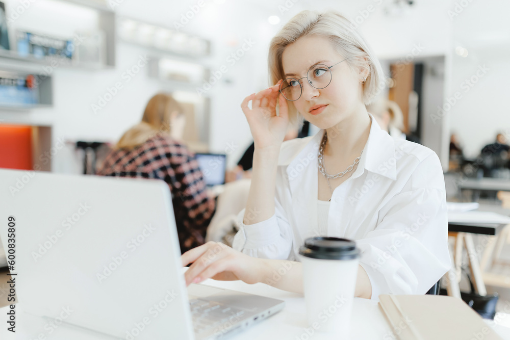 Young business woman sitting at table and taking notes in notebook. On workplace laptop, smartphone and cup of coffee. Concept student learning online. Side view blogger Young business woman sitting at table and taking notes in notebook. On workplace laptop, smartphone and cup of coffee. Concept student learning online. Side view blogger