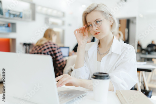 Young business woman sitting at table and taking notes in notebook. On workplace laptop, smartphone and cup of coffee. Concept student learning online. Side view blogger