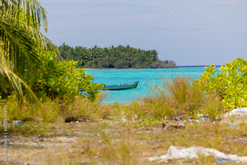 Coconut palm or trees with clear sky with clouds, and sun with traditional boats on a seaside, tropical boats or bokkuraa from Maldives islands