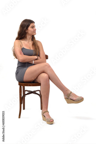 view of young girl sitting on chair arms crossed and cross legged looking away on white background