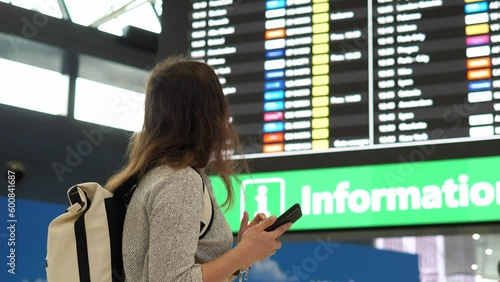 Woman stands at the airport near the flight registration board waiting for her flight.