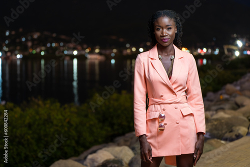 Portrait of a young black woman wearing a blazer dress standing in the city at night with city lights behind her photo